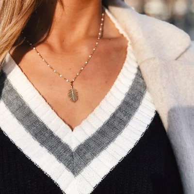 Colar com pendente de folha dourada, camisola preta com listras brancas e cinzentas em V, casaco claro