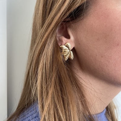 brinco dourado de folhas na orelha de mulher loira com suéter roxo