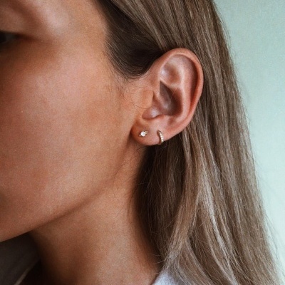 Orelha de mulher com brincos pequenos, incluindo um de pérola e um aro dourado pequeno