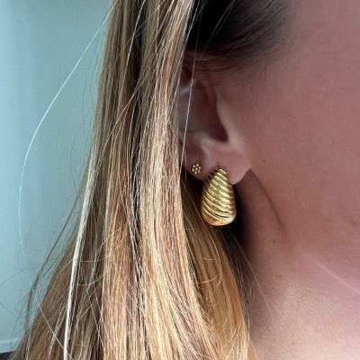 Brinco dourado em forma de concha em orelha de pessoa