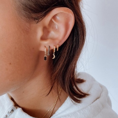 Orelha esquerda com três brincos dourados pendurados, pessoa com casaco branco