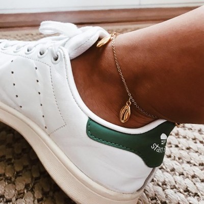 Tênis brancos com detalhe verde e pulseira dourada no tornozelo