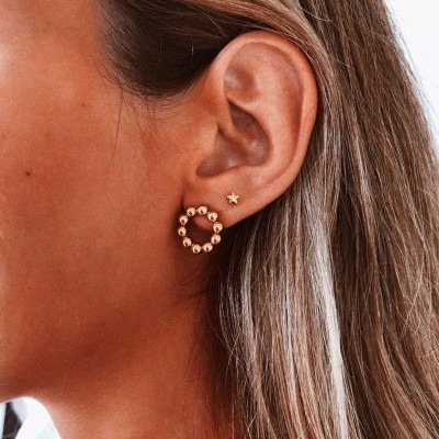 Brincos dourados em forma de estrela e círculo na orelha de uma mulher