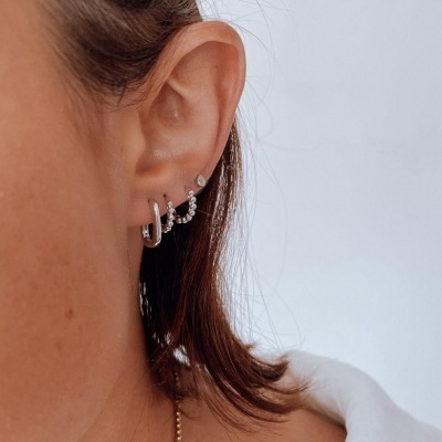 Orelha feminina com três brincos prateados e fundo branco