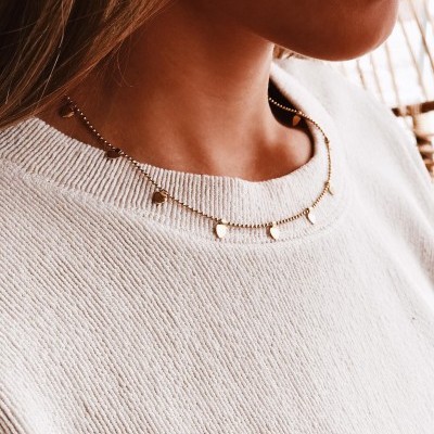 Colar dourado com pequenas contas e pendentes redondos sobre camisola branca de malha