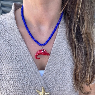 Colar azul com pendente vermelho em forma de camarão e camisola bege texturizada com botão dourado