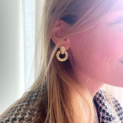 Brinco dourado torcido circular em orelha de mulher com casaco pied-de-poule