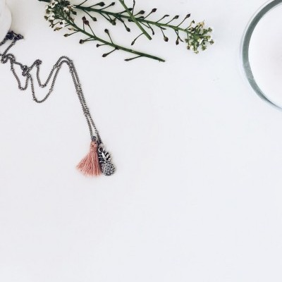 Colar com pendente de abacaxi e borla rosa em superfície branca com ramos de flores