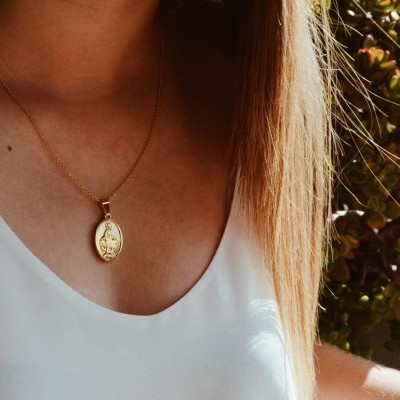 Colar dourado com pendente oval em relevo usado por pessoa com blusa branca