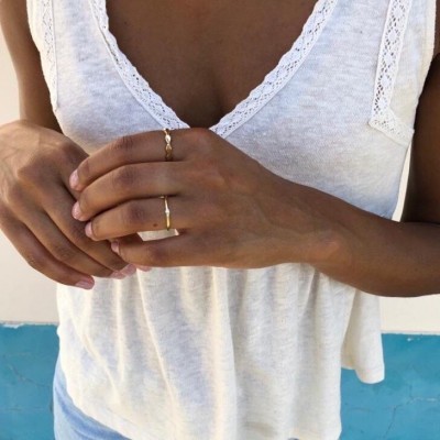 Pessoa a mostrar mãos com anéis dourados, usando top branco com renda e roupa azul clara.