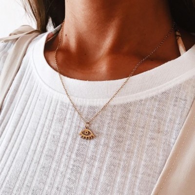 Colar dourado com pendente de olho sobre camisola branca de malha