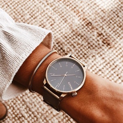 Relógio de pulso dourado com mostrador cinzento escuro e bracelete metálica no pulso