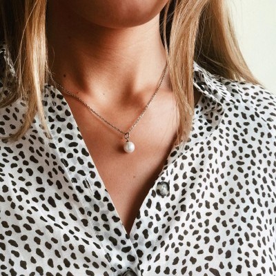 Colar com pendente de pérola em camisa branca com manchas pretas.