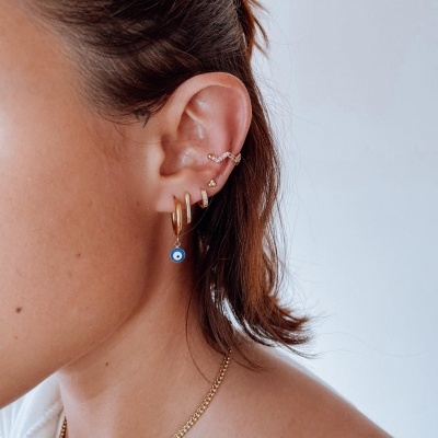 Mulher com vários brincos dourados e colar no pescoço sobre fundo branco