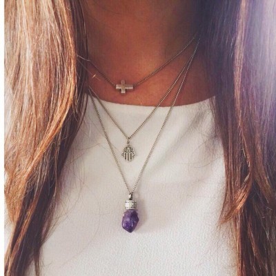 Colares prateados com cruz, mão de Fátima e pedra ametista sobre camisa branca