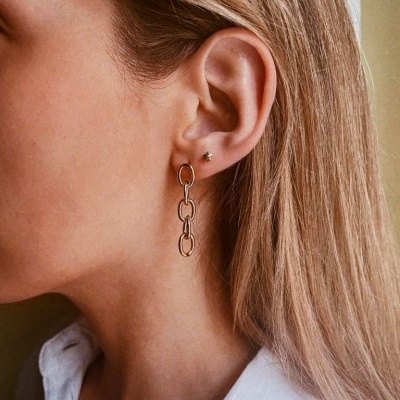 Brincos dourados de elos alongados numa mulher com cabelo loiro