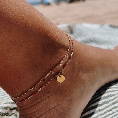 Tornozelo com duas pulseiras douradas e pendente redondo na praia
