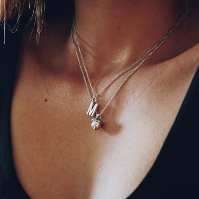 Colar duplo prateado com pingentes em letra M e esfera no pescoço de mulher com top preto