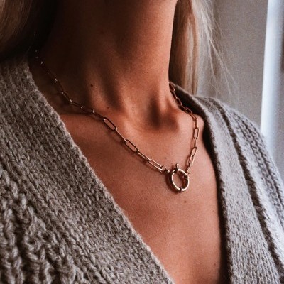 Colar dourado com corrente de elos e fecho circular num pescoço com casaco cinza de malha