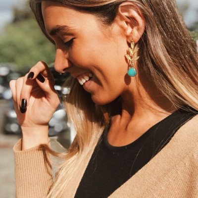 Brincos dourados com pedra turquesa em mulher sorridente ao ar livre