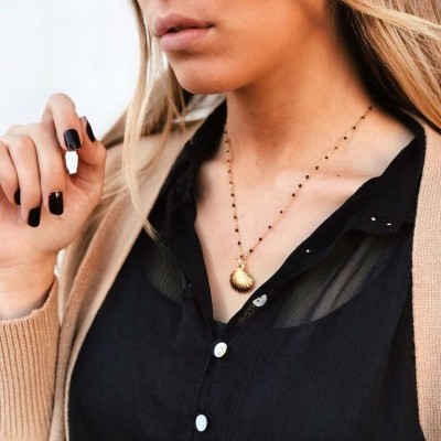 mulher com colar dourado de concha e roupa preta e bege