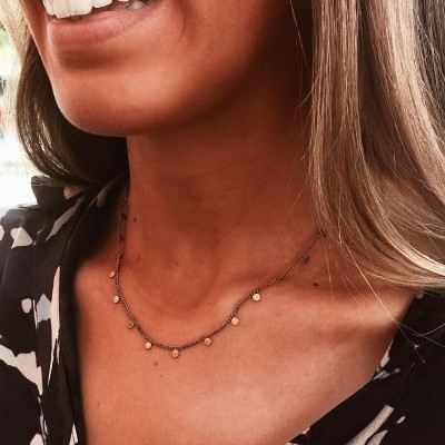 Colar delicado dourado com bolas pequenas em mulher com camisa floral preta