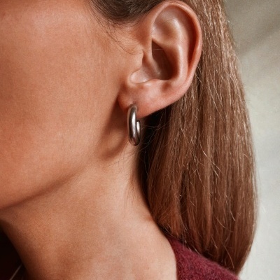 Brinco de argola prateado na orelha esquerda de pessoa com cabelo castanho