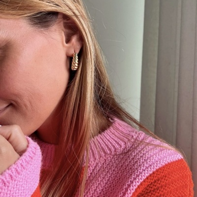 Brincos dourados trançados usados por mulher com jersey rosa e vermelho