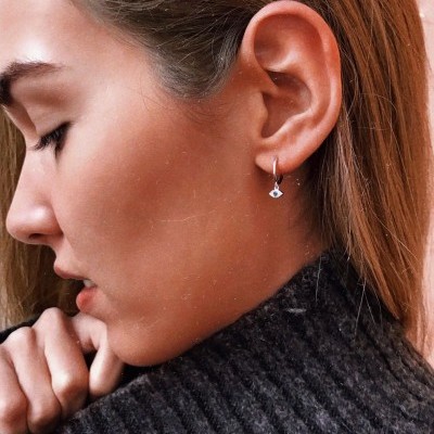 Brincos prata com pendente em forma de olho usados por mulher com camisola cinzenta