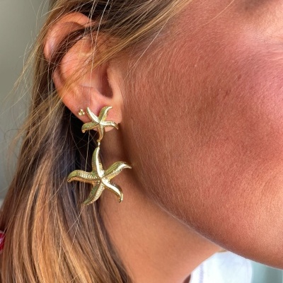 Brinco dourado com estrelas-do-mar pendentes na orelha de mulher