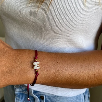 Pulseira vermelha com pendente letra M usado com roupa branca e azul