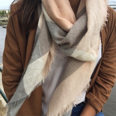 Lenço grande em padrão xadrez bege e cinza com franjas usado com casaco castanho e camisa branca junto a água