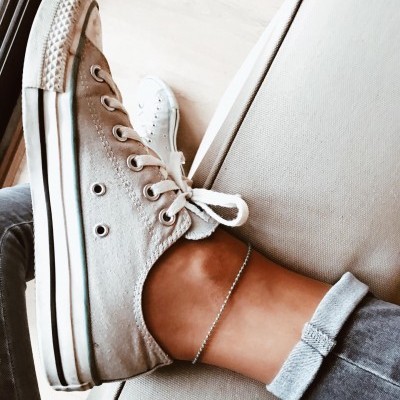 Tênis casual cinza claro com sola branca usado numa perna com calças jeans cinza enroladas