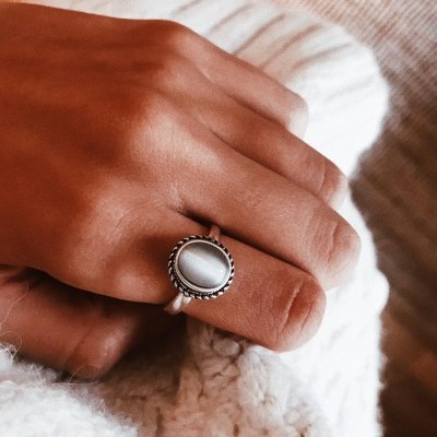 Anel de prata com pedra cinza sobre mão em roupa branca tricotada