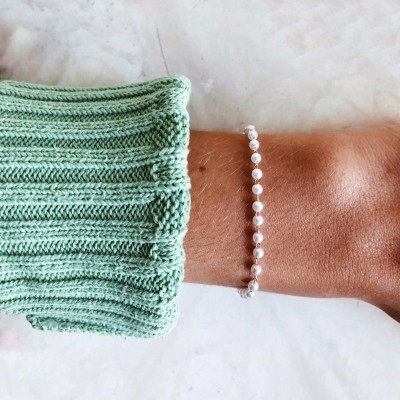 Pulseira de contas brancas redondas numa mão com manga verde de malha