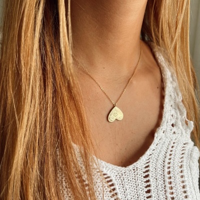 Colar dourado com pendente em forma de coração com padrão gravado usado com top de malha branco