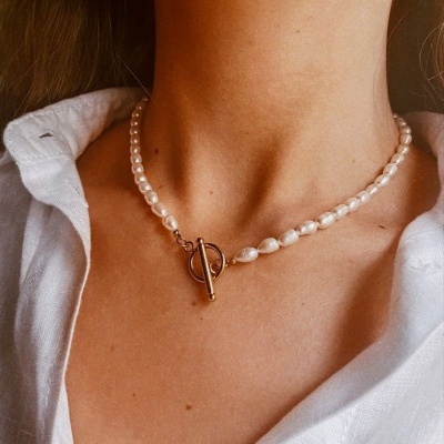 Colar de pérolas brancas com fecho metálico dourado no pescoço de pessoa com camisa branca.