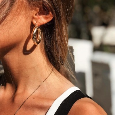 Brincos dourados de argola torcidos em mulher ao ar livre