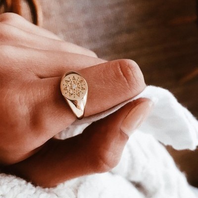 Anel dourado com estrela gravada numa mão sobre tecido branco