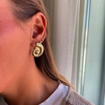 Brincos dourados em forma de concha na orelha de uma mulher