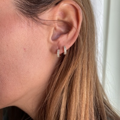 Brincos de argola prateada com pedras numa orelha feminina