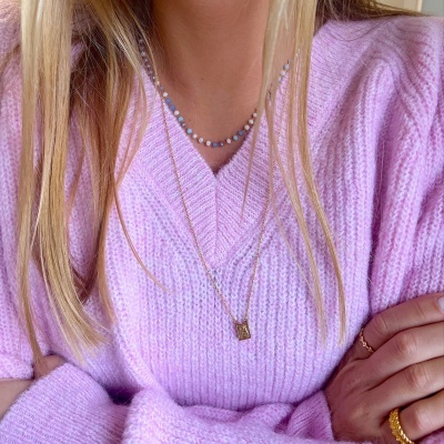 Pessoa com suéter rosa de malha grossa e colares dourado e de contas coloridas