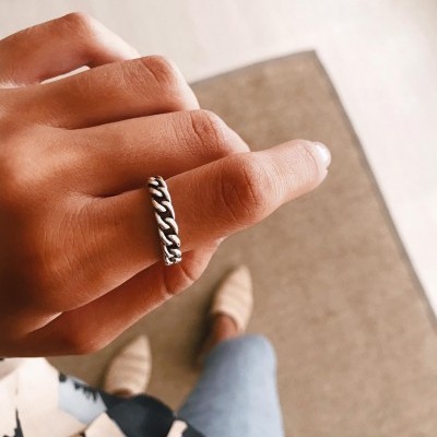 Anel prateado com padrão de elos em cadeia num dedo médio