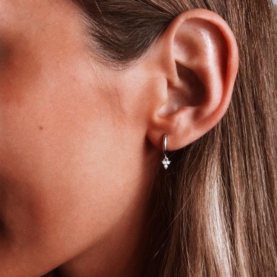 Brinco prateado pequeno com pedras pendurado na orelha direita de uma pessoa