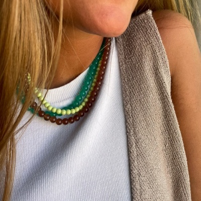 Colar triplo de contas esféricas coloridas usado por mulher com camisa branca e colete cinza-bege