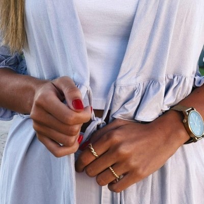 Mãos femininas segurando peça de roupa azul clara com folhos e acessórios dourados e castanhos