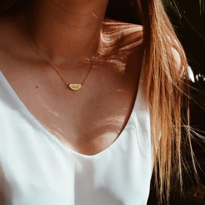 Colar dourado com pendente recortado em forma de meio círculo sobre pele, com camisa branca