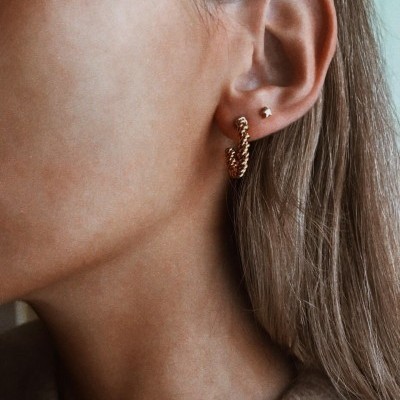 Orelha feminina com dois brincos dourados, um pequeno e outro em argola trançada.