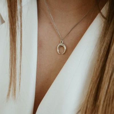 Colar prateado com pendente em forma de ferradura usado com camisa branca