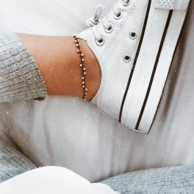 Ténis branco com riscas pretas e pulseira prateada no tornozelo